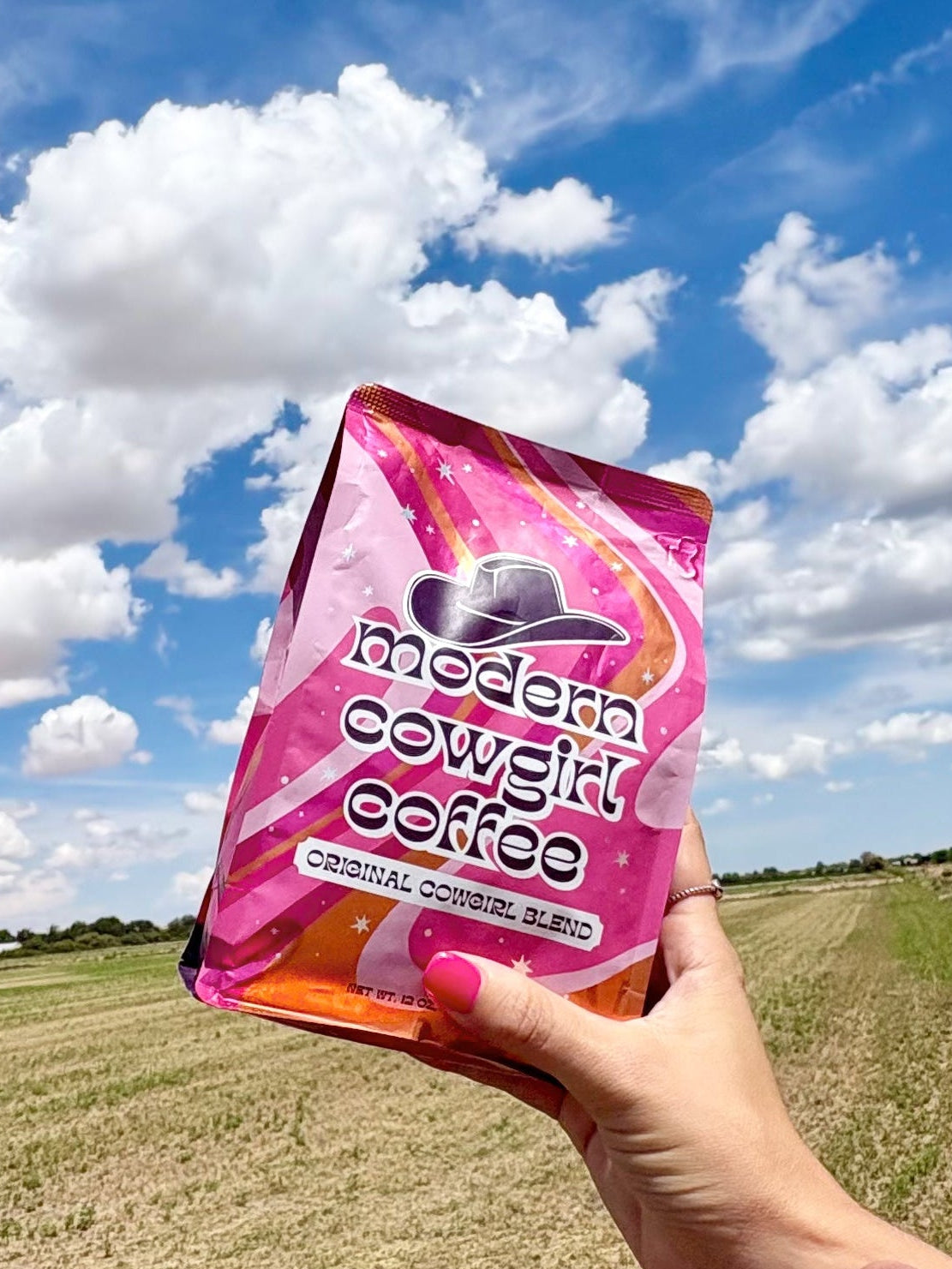 Pink Modern Cowgirl Coffee bag held against a wide blue sky